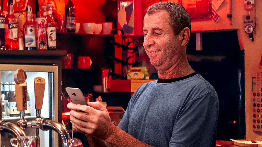 Central European Guy At Other End Of Bar Watching Some Sport With Mallets On Phone